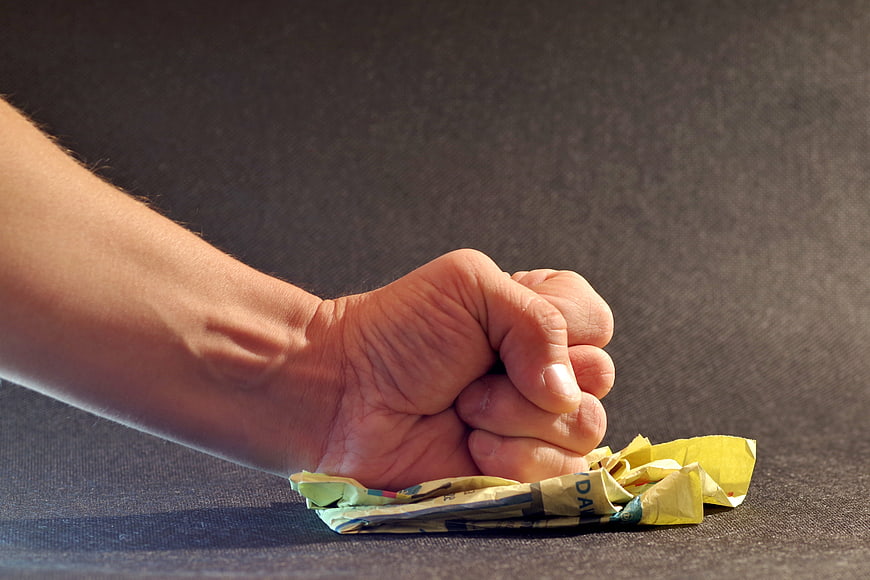 Angry Fist Crushing Crumpled Paper on Dark Surface
