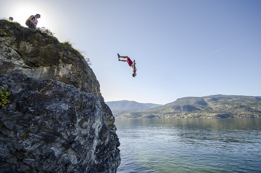 Man cliff diving into lake with mountains background