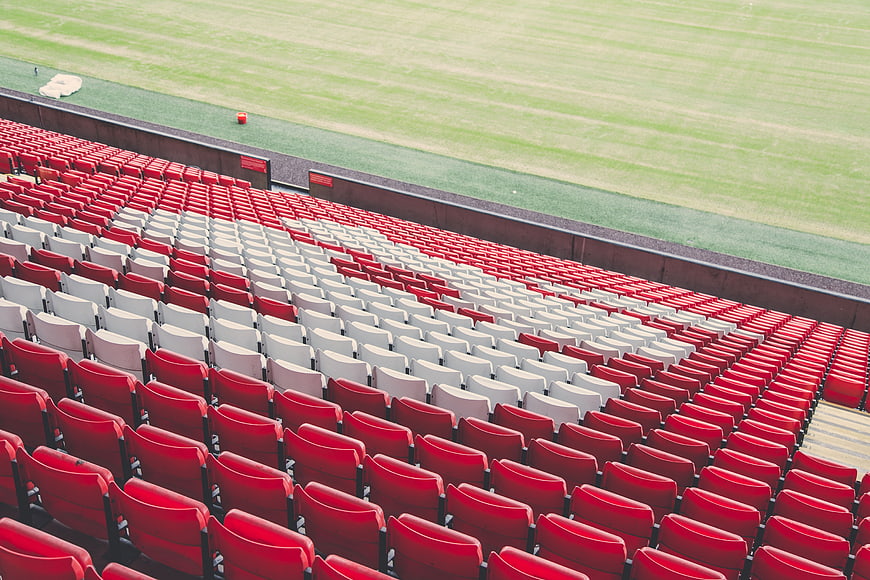 Empty red and white stadium seats overlooking a green field
