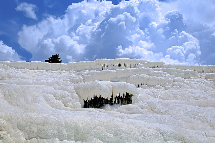 White travertine terraces with icicles under blue sky