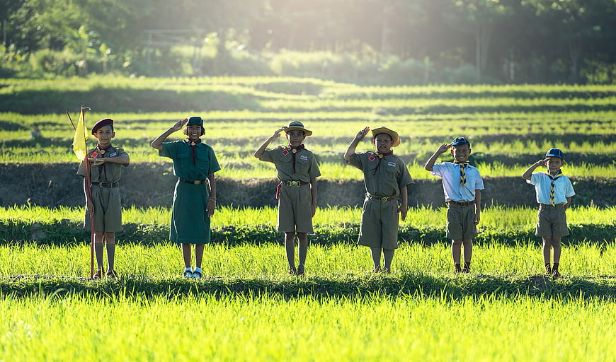 Group of young scouts saluting in a green rice paddy field