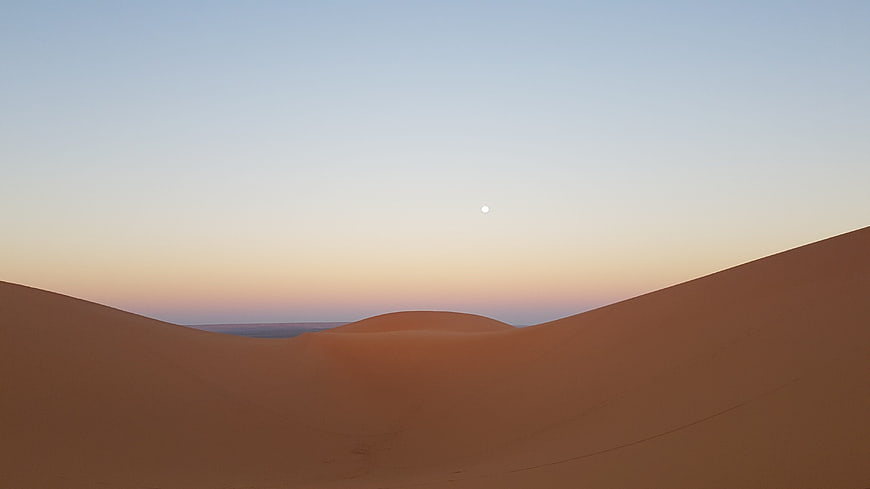 Serene Desert Dunes at Sunset with Moon in Sky