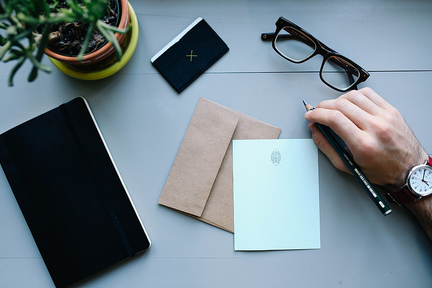 Man writing letter on desk with notebook and glasses