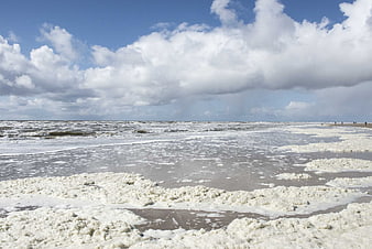 Foamy white sea foam on sandy beach under cloudy sky