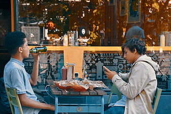 Two boys sitting at outdoor cafe table with food and drinks