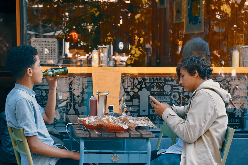 Two boys sitting at outdoor cafe table with food and drinks