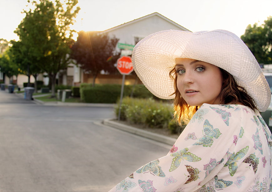 Woman in White Sun Hat on Suburban Street at Sunset