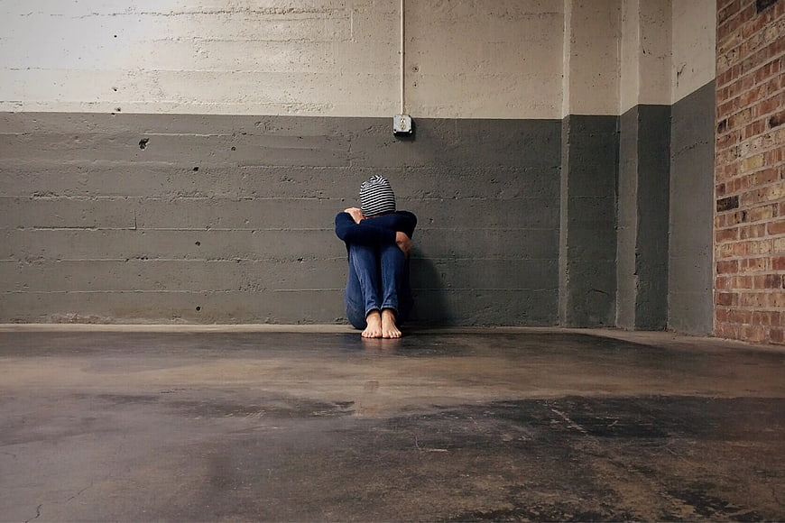 Lonely Person Sitting Against Wall in Empty Industrial Room