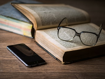 Open book with glasses and smartphone on wooden table