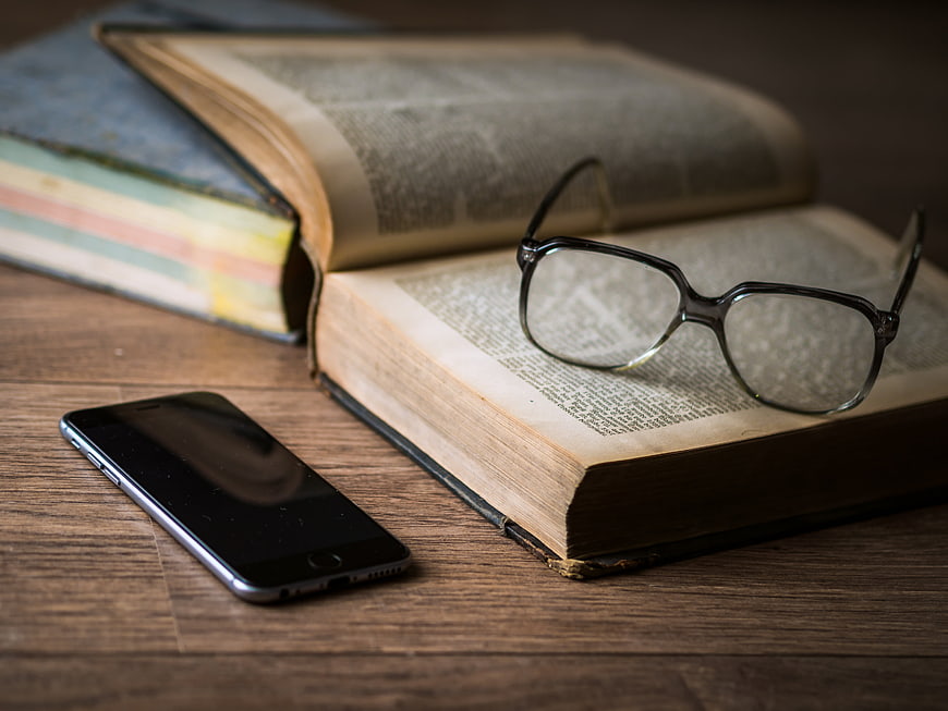 Open book with glasses and smartphone on wooden table