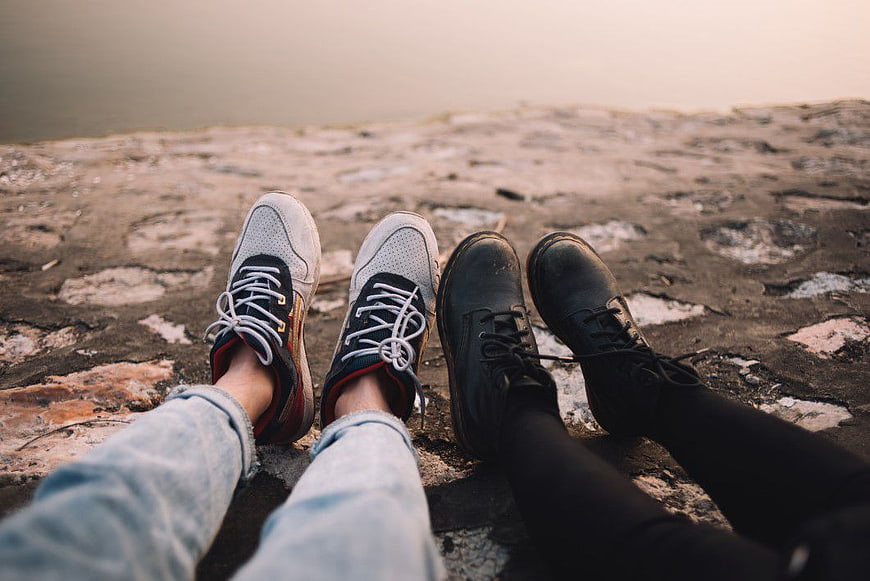 Couple's feet in sneakers and boots sitting by water