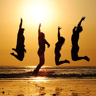 Silhouettes of friends jumping on beach at sunset