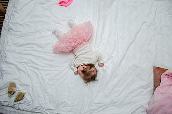 Top view of sleeping baby girl in pink tutu on white bed