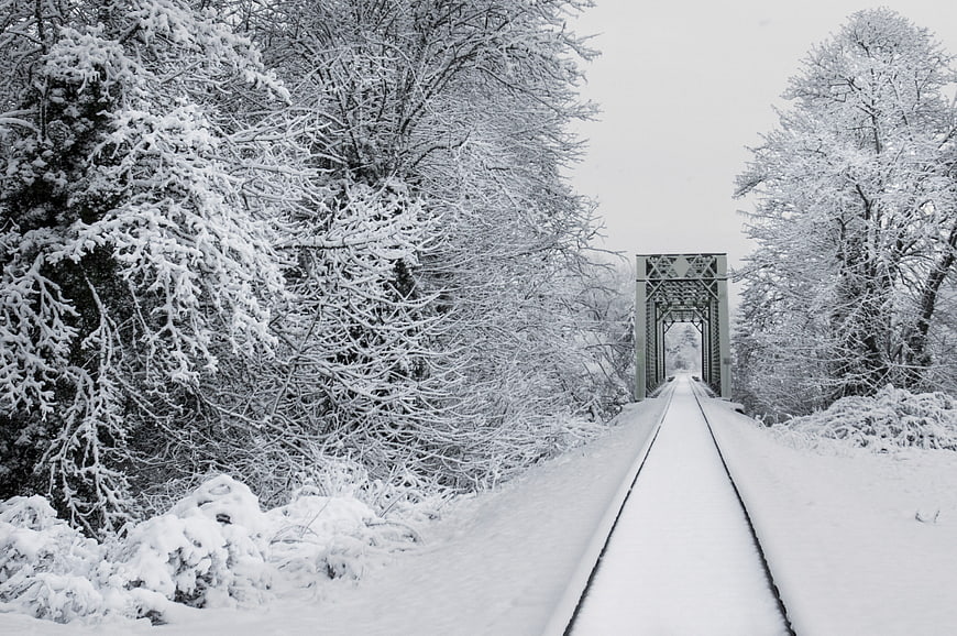 Snow-covered railway tracks leading to a bridge in winter