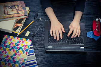 Top view of hands typing on laptop with study supplies