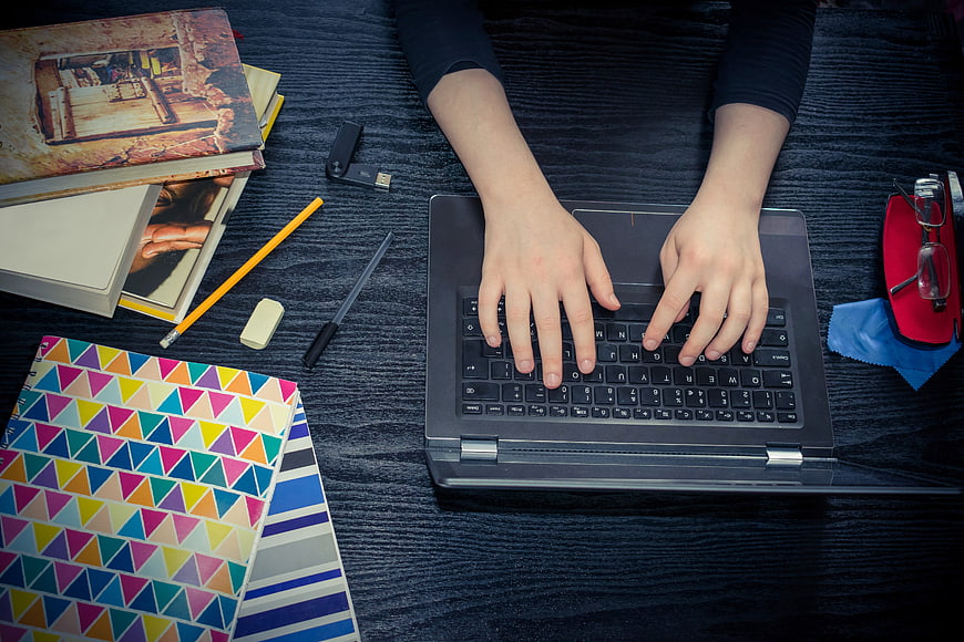 Top view of hands typing on laptop with study supplies
