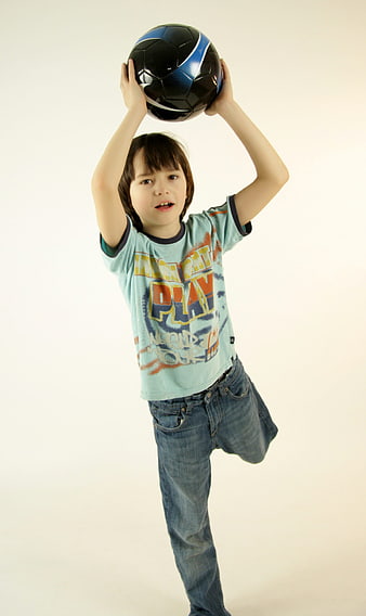 Young boy holding soccer ball above head in studio