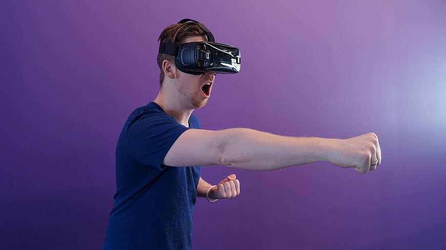 Man Wearing VR Headset Punching Against Purple Background