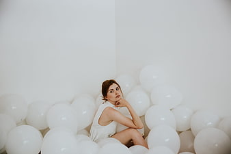Young woman sitting in a pile of white balloons in a minimalist studio