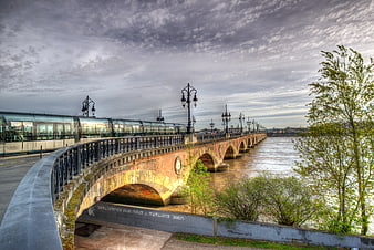 Modern tram crossing historic stone bridge over river