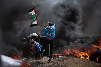 Palestinian Protesters With Flag Amidst Fire And Smoke