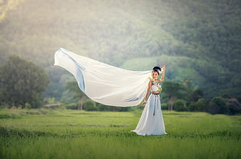Elegant Asian Woman in White Dress with Flowing Fabric in Green Field