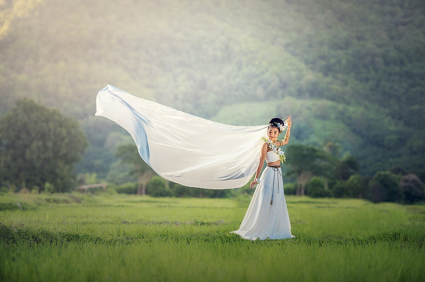 Elegant Asian Woman in White Dress with Flowing Fabric in Green Field
