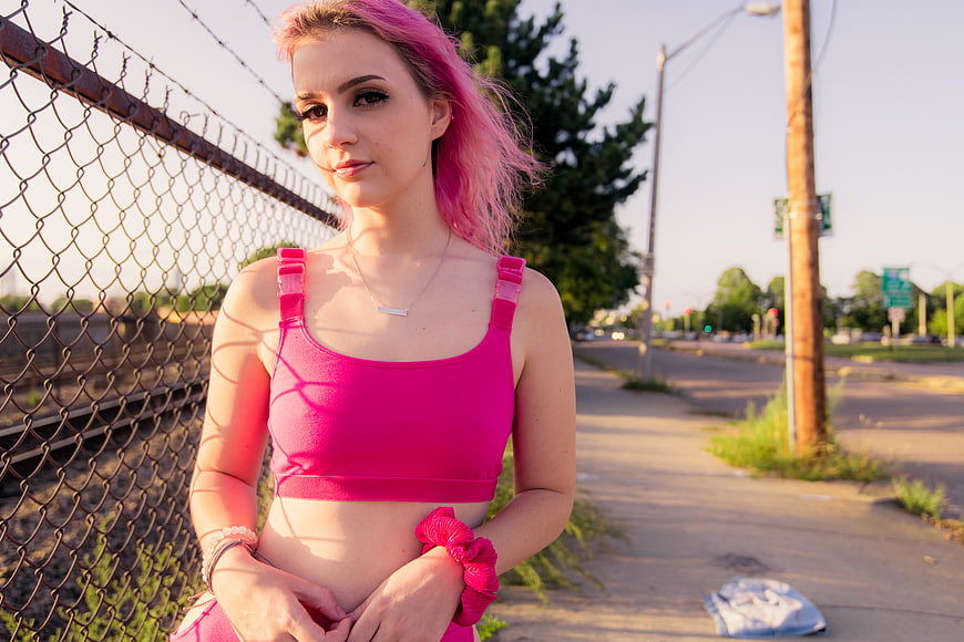 Young woman with pink hair and fitness outfit by fence