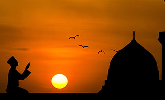Silhouette of Muslim man praying at sunset near mosque dome