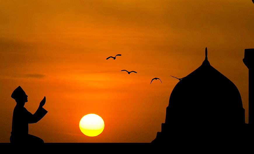 Silhouette of Muslim man praying at sunset near mosque dome
