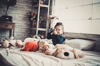 Cute Toddler Girl Taking Photos with Vintage Camera on Bed