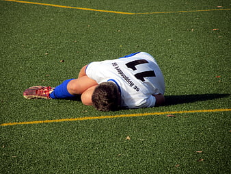 Young soccer player lying on green artificial turf field