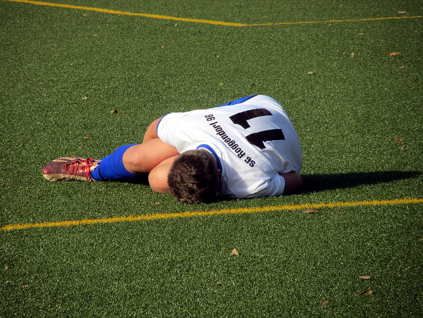 Young soccer player lying on green artificial turf field