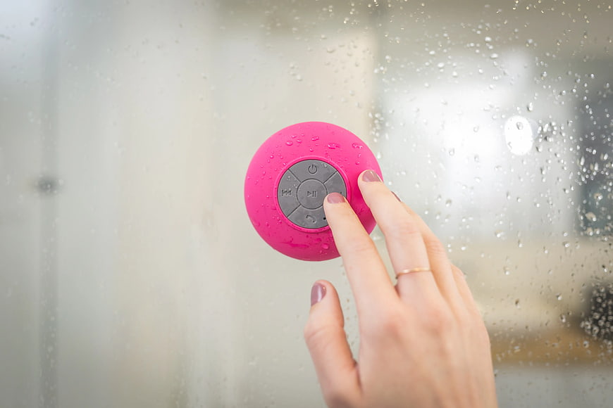 Woman pressing pink waterproof shower speaker button