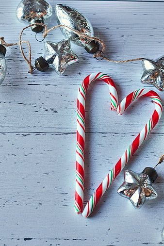 Candy Canes Forming Heart Shape with Silver Ornaments on Wood