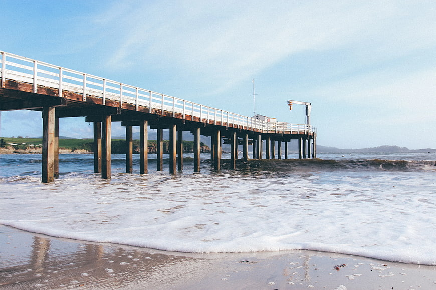 Wooden pier extending over ocean waves on a sunny day