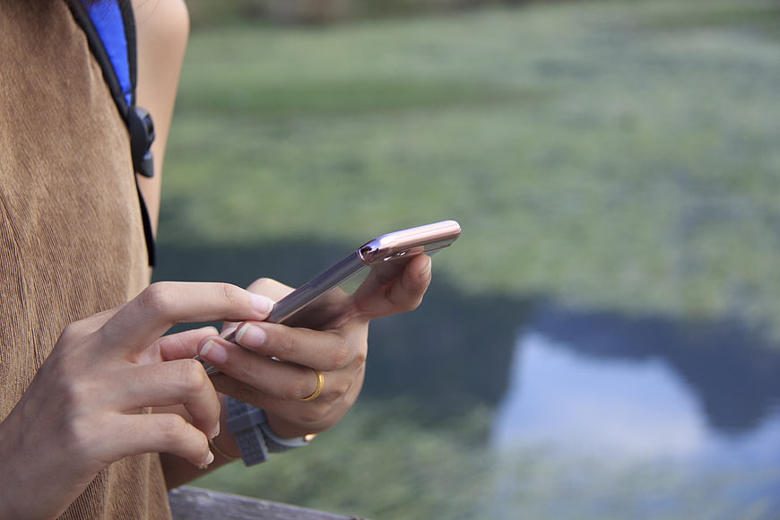 Close-up of hands using smartphone outdoors by water