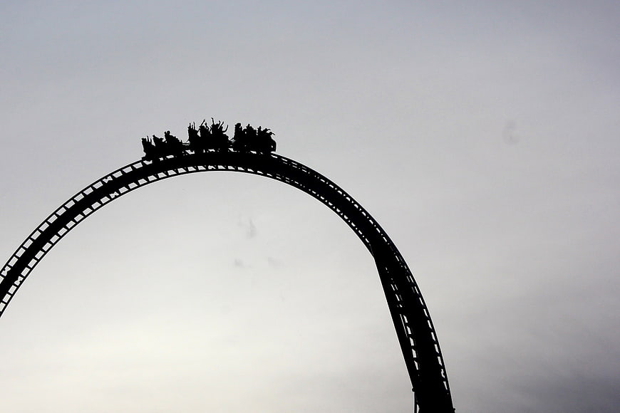 Silhouette of roller coaster car on track arch against gray sky