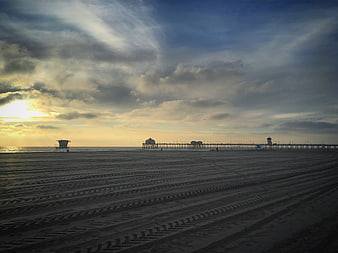 Dramatic sunset over beach with pier and tire tracks