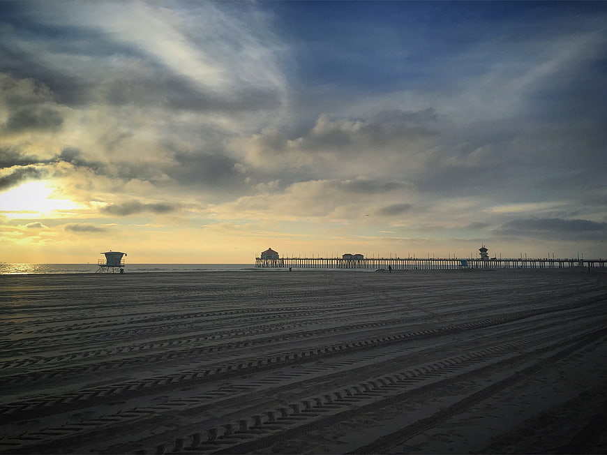 Dramatic sunset over beach with pier and tire tracks