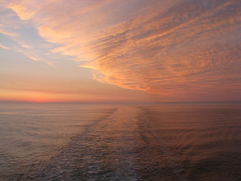 Sunset over ocean with boat wake and orange clouds