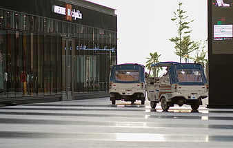 Two white tuk-tuks parked outside modern shopping mall