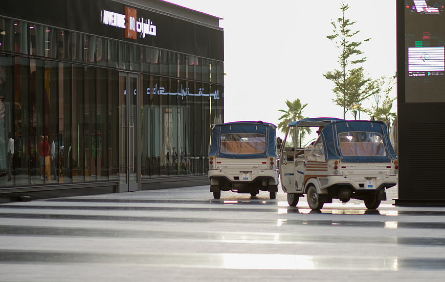 Two white tuk-tuks parked outside modern shopping mall