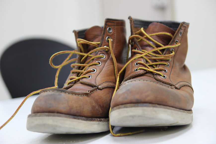 Well-worn brown leather work boots with yellow laces on white surface