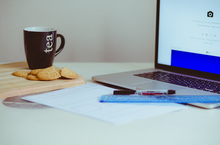 Laptop workspace with tea mug and cookies on desk