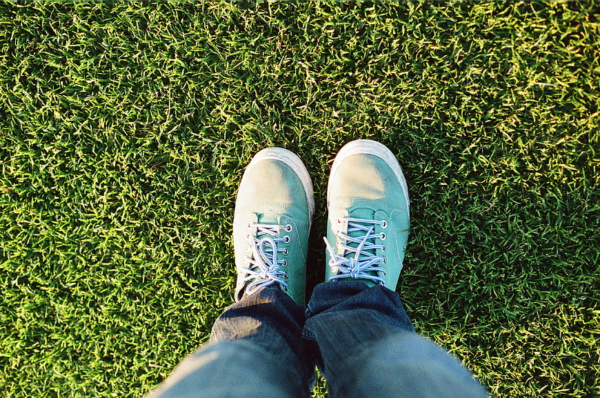 First-person view of turquoise sneakers on green grass