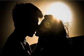Silhouette of a couple kissing against a bright sunset