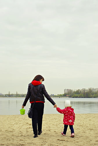 Mother and daughter walking hand in hand on sandy beach