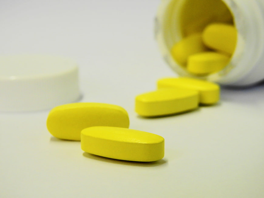 Yellow oval pills spilling from white bottle on white background