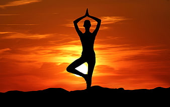 Silhouette of woman doing yoga tree pose at sunset